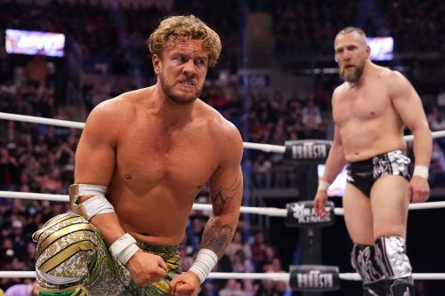 Will Ospreay kneels in the foreground, looking over his left should at Bryan Danielson.