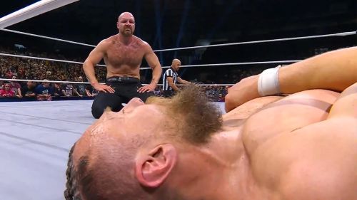 Jon Moxley kneels in the wrestling ring while looking at a prone Bryan Danielson.