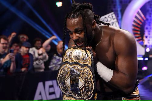 Swerve Strickland holds the AEW World Championship under his chin. Fans cheer in the background.