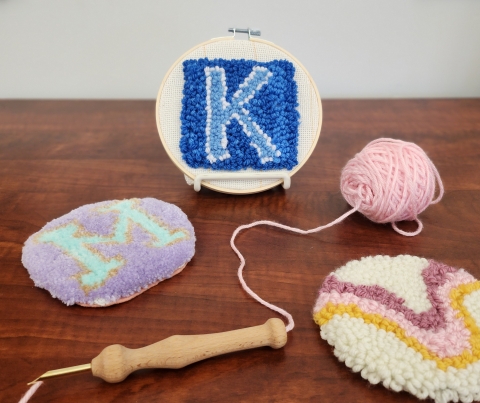 Assortment of three punch needle coaster designs, a punch needle tool and a ball of yarn.